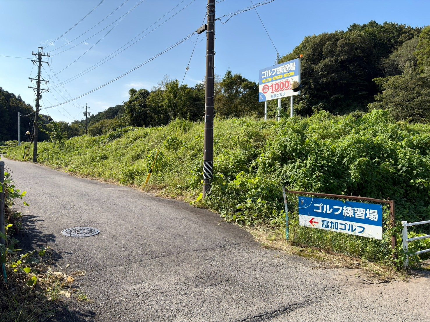 道の角に立つ「ゴルフ練習場 ← 富加ゴルフ」の小さな案内看板。左に入る細い道がある